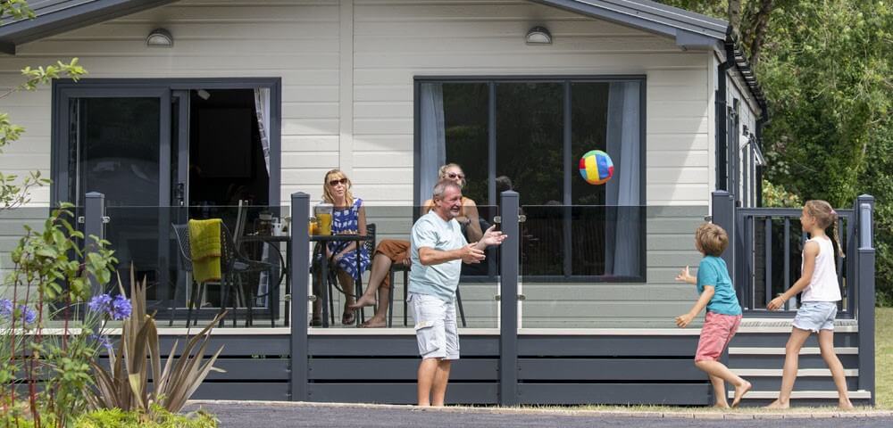 Family plays with a beach ball outside Woodland Glade luxury holiday lodge in Hoburne Devon Park